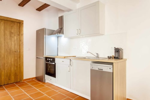 Cocina moderna del apartamento Rustikalpuente con muebles blancos, electrodomésticos de acero inoxidable y piso de baldosa terracota.