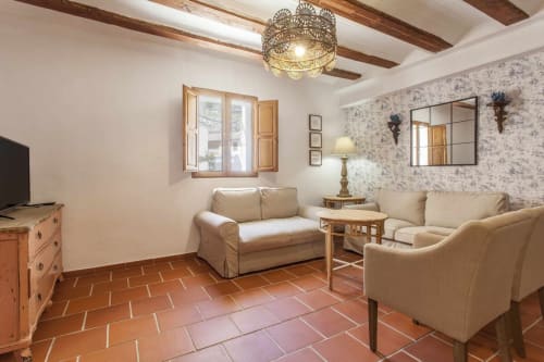 Sala de estar rústica con muebles beige, baldosas de terracota, vigas de madera e iluminación decorativa