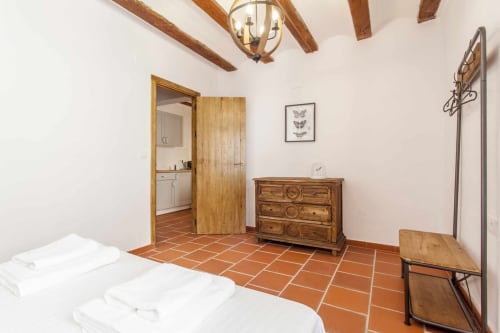 Dormitorio de apartamento rústico con baldosas de terracota, vigas de madera, cómoda y acceso a baño privado en