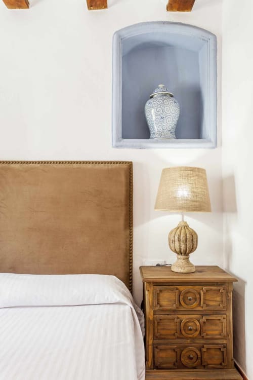 Dormitorio en Rustikalpuente con cabecera tapizada en tonos beige, mesita de noche de madera, lámpara de ratán y nicho azul con jarrón decorativo