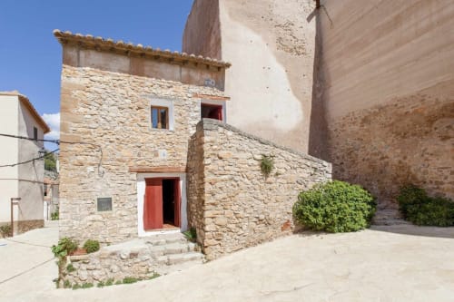 Fachada de piedra histórica en Rustikalpuente con puerta roja y hiedra, arquitectura española tradicional