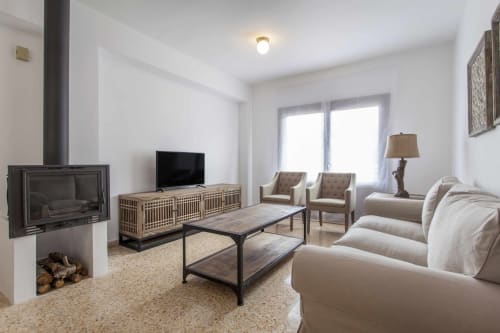 Sala de estar del apartamento Rustikalpuente con chimenea, sofá crema, mueble TV de madera, mesa de centro moderna y puertas de vidrio