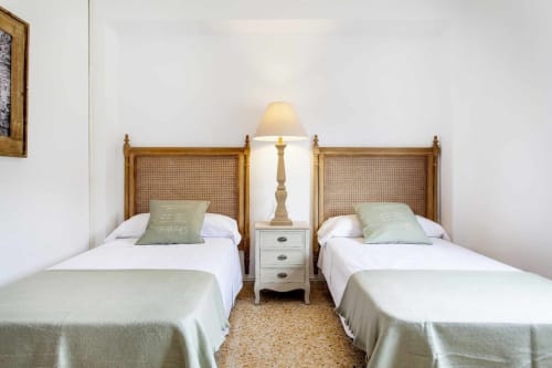Dormitorio doble con cabeceras de ratán tejido, sábanas blancas y almohadas verdes en apartamento Rustikalpuente