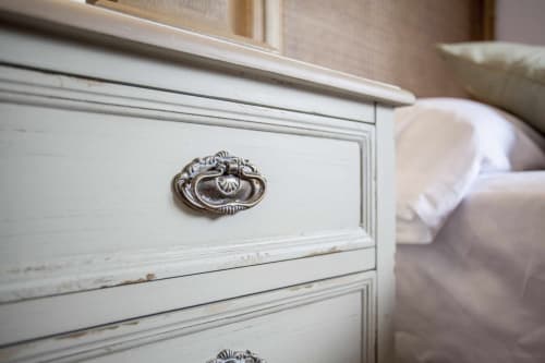 Mesita de noche blanca desgastada con herrajes plateados ornamentales en dormitorio de apartamento Rustikalpuente