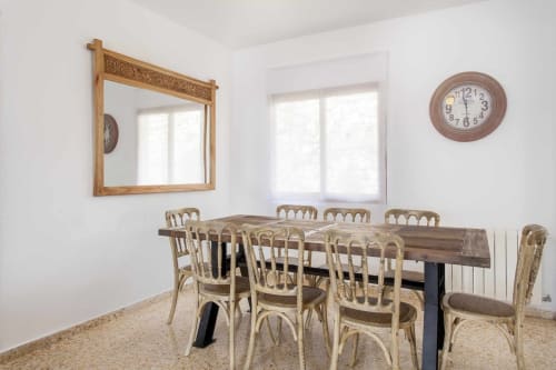 Comedor luminoso con mesa de madera, sillas tejidas, espejo ornamentado y reloj de pared en el apartamento Rustikalpuente