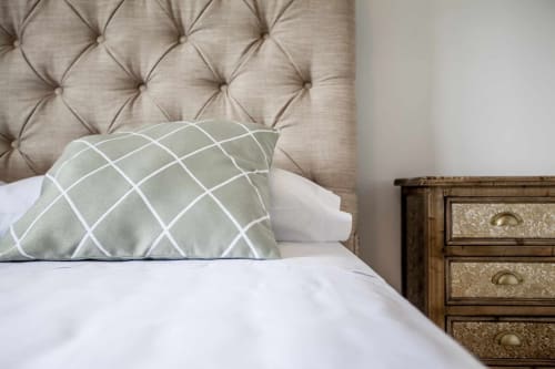 Acogedora habitación en Rustikalpuente con cabecero capitonado beige, almohada con patrón geométrico y mesilla de noche de madera.