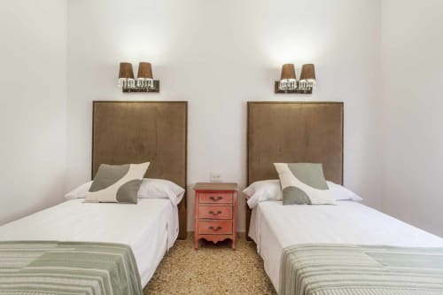 Dos camas individuales con cabeceros tapizados en marrón en el apartamento Rustikalpuente, España, separadas por una mesita de noche roja