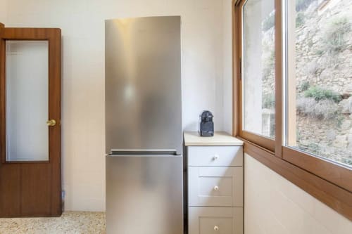 Cocina moderna con refrigerador de acero inoxidable, gabinetes blancos y amplias ventanas con vista al exterior de piedra