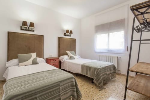Dormitorio luminoso en Rustikalpuente con dos camas individuales, cabeceros marrones, mantas rayadas y luz natural de ventanas