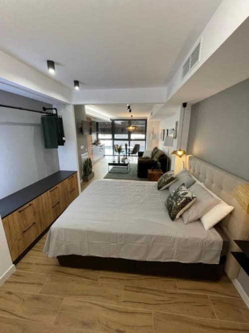 Moderno apartamento estudio en Alicante con cama de matrimonio, cómoda de madera, TV y vistas a la ciudad desde el balcón