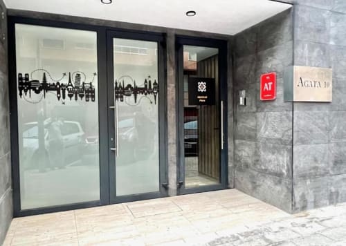 Entrada de Agata 10 Apartamentos en Alicante con puertas de cristal decoradas con diseño de skyline de la ciudad y señalización