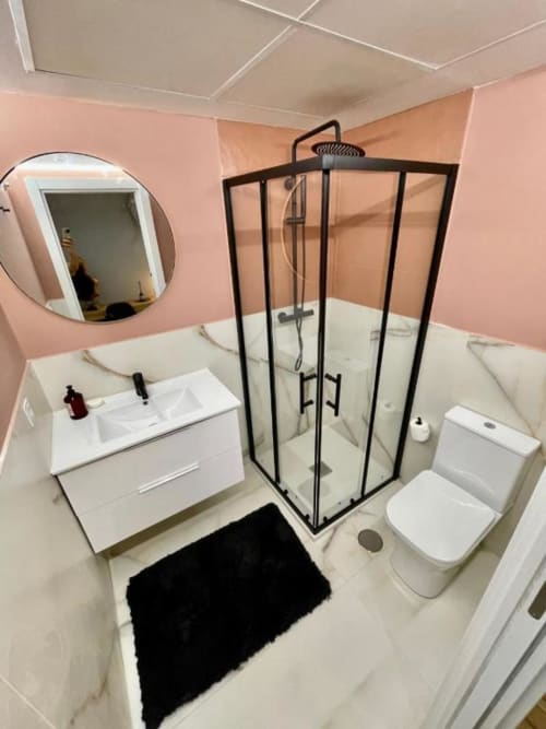 Baño moderno en Agata 10 Apartamentos, Alicante con ducha de marco negro, tocador blanco, inodoro y paredes rosa