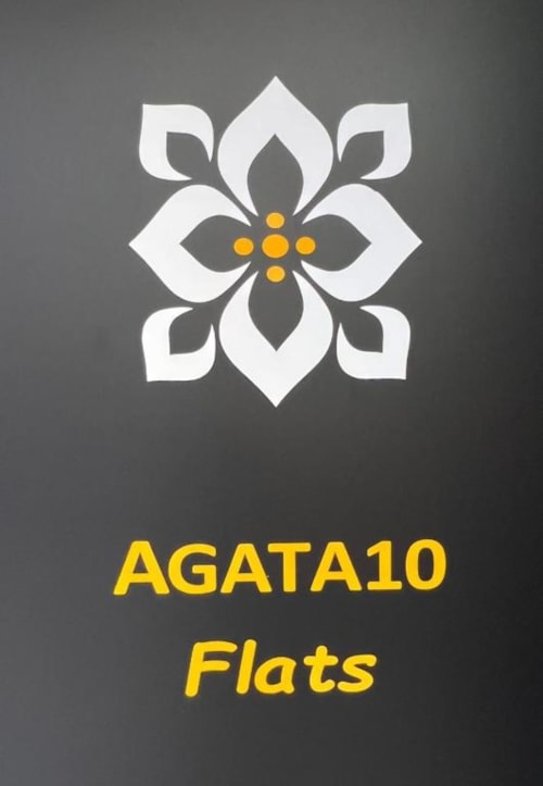 Logotipo de Agata10 Flats con flor blanca decorativa y centro dorado sobre fondo gris