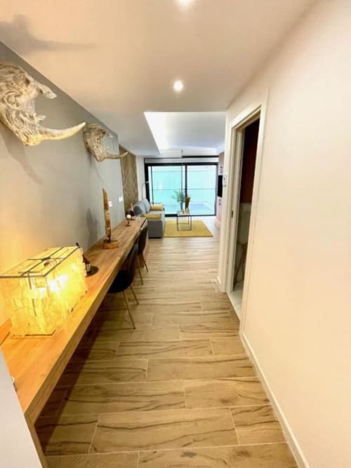 Pasillo moderno de apartamento en Alicante con suelos de madera, escritorio y vistas de la ciudad por las ventanas