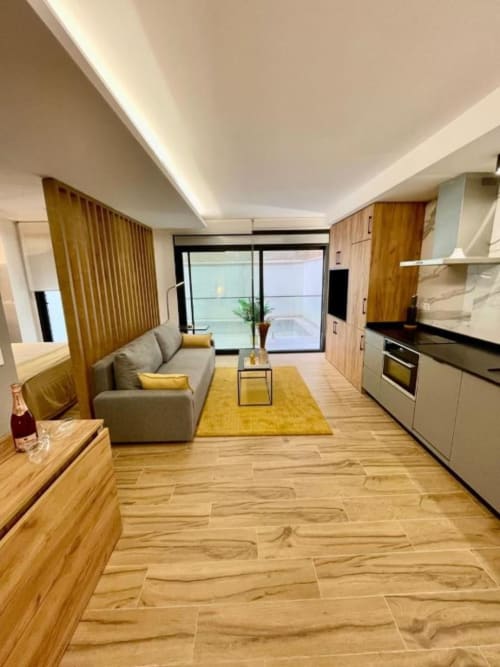 Salón moderno en Alicante con sofá gris, detalles en amarillo, suelos de madera y vistas a la ciudad en Agata 10