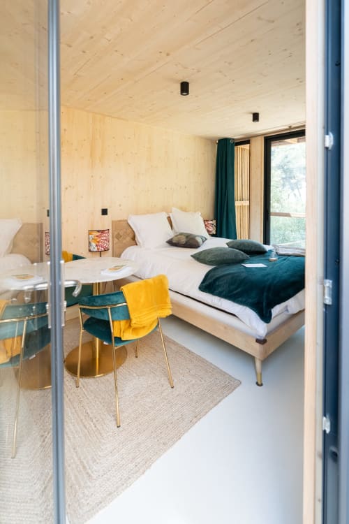 Modern lodge bedroom at Le chant des pins with wooden walls, teal accents, and yellow chair in Saint-Marc-Jaumegarde