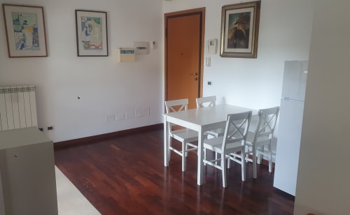Moderna cucina e zona pranzo di un appartamento a Roma con tavolo bianco, quattro sedie, frigorifero e zona living