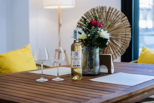 Mesa de comedor elegantemente ambientada en Ab Be Apartments Málaga con vino, copas, flores frescas y vistas al mar