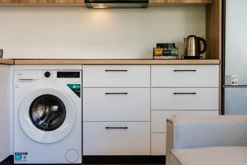 Moderna cocina de apartamento en Málaga con lavadora Candy blanca, muebles y hervidor de acero inoxidable en la encimera