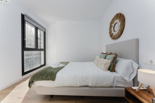 Dormitorio moderno en Ab Be Apartments, Fuengirola, con cama tapizada gris, ropa de cama blanca y vistas al mar