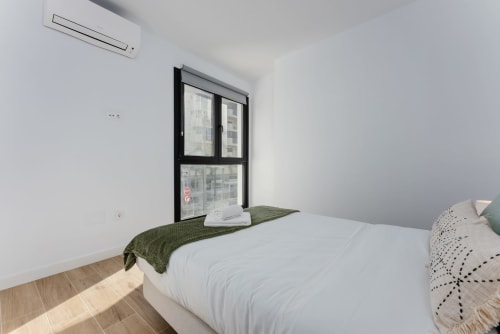Dormitorio moderno en Ab Be Apartments, Fuengirola con vistas al mar, cama blanca, manta verde, marco de ventana negro, suelo de madera