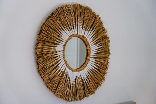 Espejo decorativo de paja tejida con forma de sol y centro reflectante ovalado en pared blanca de apartamento en Málaga