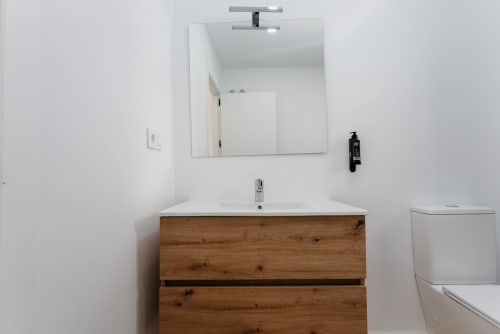 Baño moderno con vanidor de madera, lavamanos blanco, espejo iluminado, inodoro y accesorios de pared en Ab Be Apartments