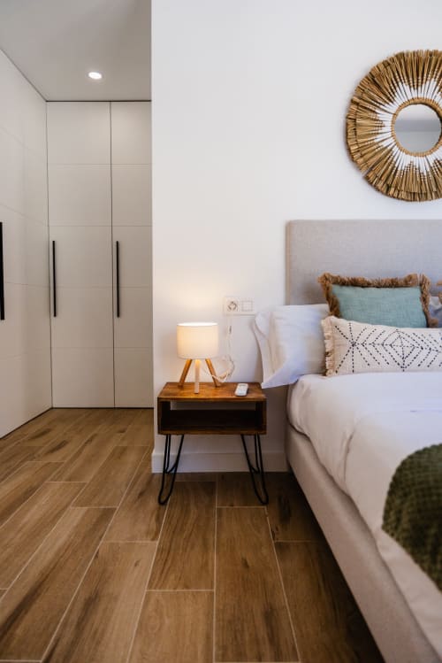 Dormitorio moderno en apartamento de Fuengirola con cama, mesita de noche de madera, lámpara, armario blanco y espejo de paja