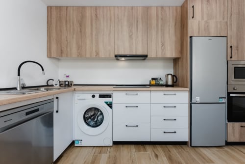 Cocina moderna en apartamento de Málaga con armarios blancos, encimeras de madera, electrodomésticos de acero inoxidable y lavadora