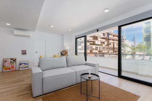 Salón moderno en Fuengirola con sofá gris, balcón con vistas al mar y paisaje costero a través de grandes ventanales