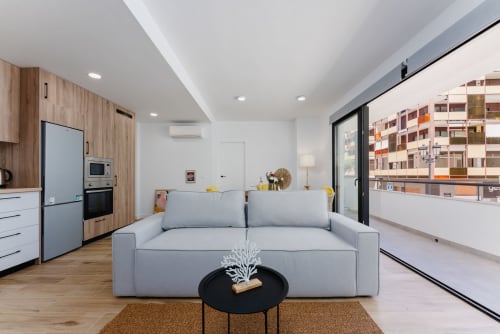 Moderno salón con sofá gris, balcón con vistas al mar, cocina de madera y vistas a Fuengirola en Málaga