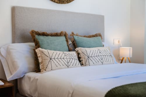 Dormitorio elegante en Ab Be Apartments de Málaga con cabecero tapizado gris y almohadas turquesas con flecos