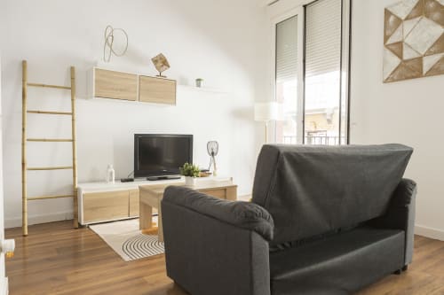 Moderno apartamento estudio en Ab Be Apartments de Málaga con sofá oscuro, mueble de TV de madera y vistas a la ciudad desde el balcón