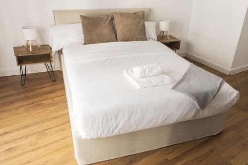 Dormitorio moderno en Ab Be Apartments de Málaga con ropa de cama blanca, almohadas marrones, mesitas de madera y piso de parqué