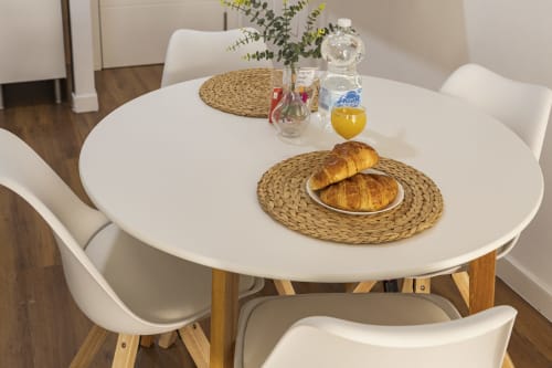 Desayuno moderno en Ab Be Apartments Málaga con croissants, zumo de naranja y flores frescas sobre mesa redonda blanca
