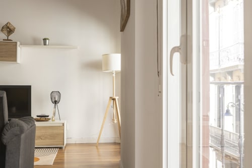 Moderno estudio en Ab Be, Málaga, con lámpara de trípode de madera, TV y vista urbana luminosa desde el balcón