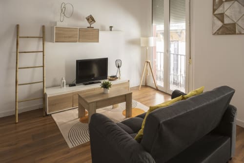 Moderno estudio en Ab Be Apartments, Málaga, con sofá oscuro, mueble TV de madera y puertas balconeras con vistas a la ciudad
