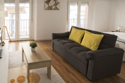 Moderno estudio en Málaga con sofá negro, cojines amarillos, muebles de madera y puertas al balcón con vistas a la ciudad