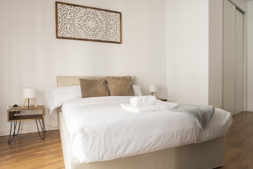 Dormitorio de estudio moderno en Ab Be Apartments, Málaga, con ropa de cama blanca, mesilla de noche de madera y decoración de arte mural