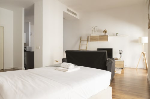 Moderno estudio en Ab Be Apartments de Málaga con cama blanca, sillón negro, pisos de madera y decoración minimalista