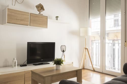 Sala de estar de estudio moderno con televisor, muebles de madera y vista a la ciudad desde el balcón de Ab Be Apartments en Málaga