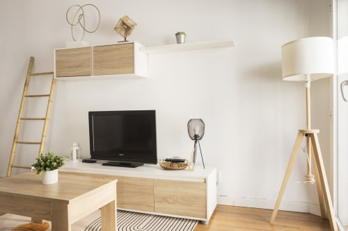 Moderno espacio de trabajo en suite de hotel con televisor, escritorio de madera, lámpara de pie y estanterías decorativas en Málaga