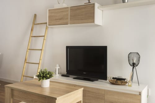 Área de estar de estudio moderno con TV de pantalla plana, escritorio de madera, escalera decorativa y planta en maceta en Ab Be