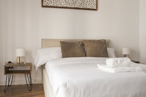 Dormitorio moderno en Ab Be Apartments Málaga con ropa de cama blanca, almohadas marrones, mesita de noche de madera y diseño minimalista