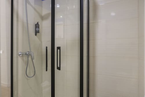 Moderno baño con ducha de obra, mampara de cristal y marcos negros en estudio Ab Be Apartments, Málaga