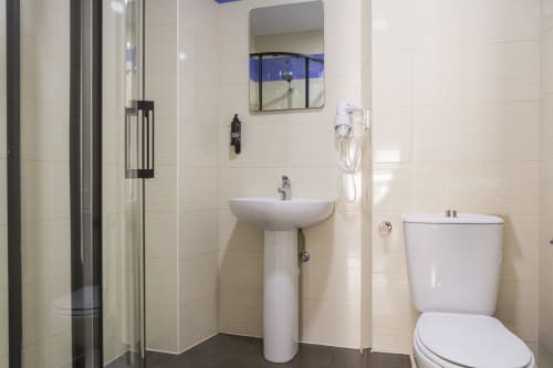 Baño moderno en estudio de Ab Be Apartments Málaga con lavamanos pedestal, inodoro, ducha, espejo y paredes de azulejos blancos