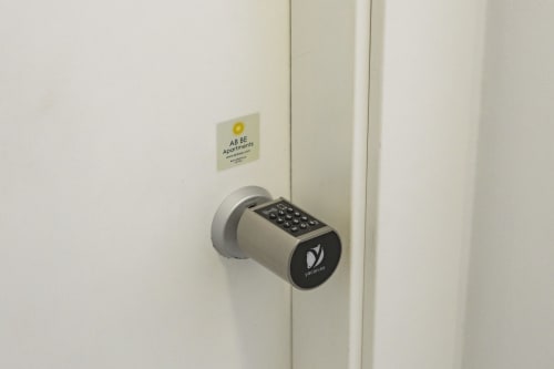 Teclado de cerradura inteligente en puerta blanca del apartamento en Ab Be Apartments, Málaga, con letrero del edificio arriba