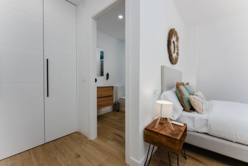 Modern bedroom at Ab Be Apartments Málaga with bed, wooden nightstand, woven wall art, and ensuite bathroom visible through