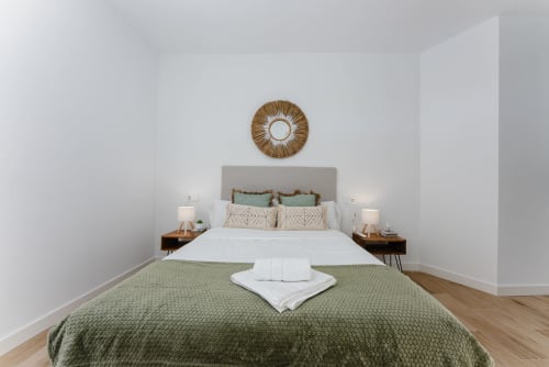 Moderna habitación en Ab Be Apartments de Málaga con cama queen, cabecero gris, ropa de cama verde, mesitas de madera y circular