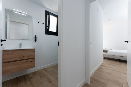 Baño moderno con tocador de madera, espejo, marco de ventana negro y vista hacia el dormitorio en Ab Be Apartments, Málaga